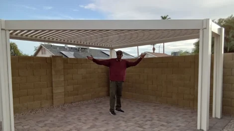 Man standing under a partially covered outdoor patio with open arms.